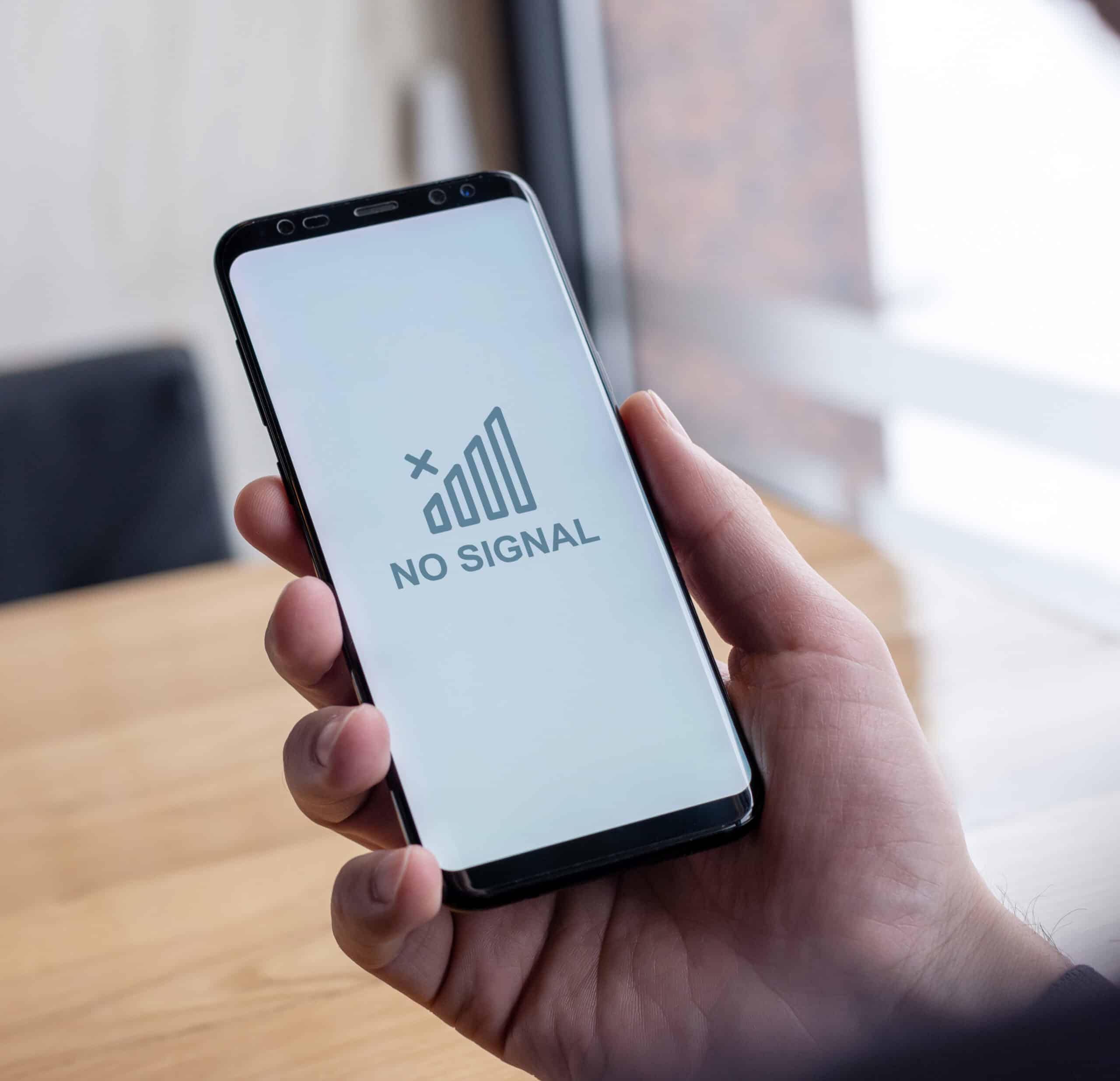 person holding a mobile device with a no signal graphic on the screen